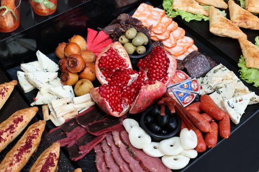 Plateau d'amuse-bouches apéritifs avec feuilletés, fromages, charcuterie, olives et fruits.