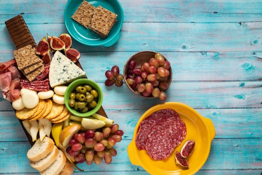 Plateau de charcuterie avec fromages, fruits, crackers et pain sur une table en bois bleu. Idéal pour un apéritif gourmand.