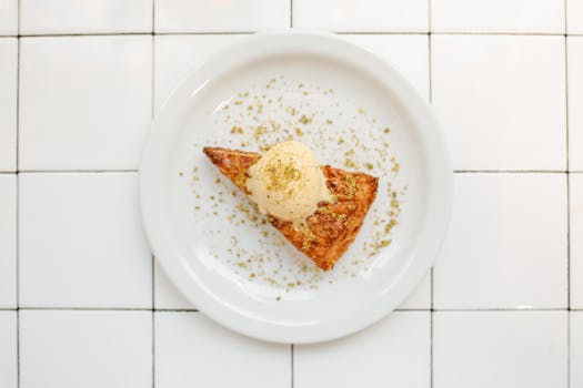 Une part de galette des rois à la pistache avec une boule de glace sur une assiette blanche.