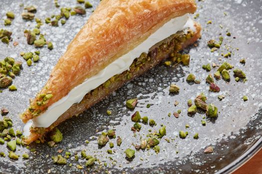 Partie de galette des rois à la pistache, garnie de crème et parsemée de pistaches concassées sur une assiette.